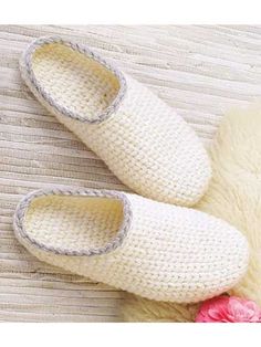 a pair of white slippers sitting on top of a wooden floor next to a pink flower