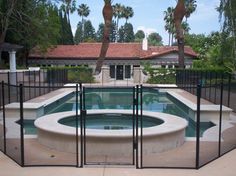 a pool surrounded by fenced in area with palm trees and a house behind it