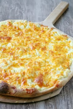 a pizza sitting on top of a wooden cutting board next to a spatula filled with cheese