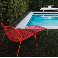 two red chairs sitting next to a swimming pool in a backyard with grass and bushes