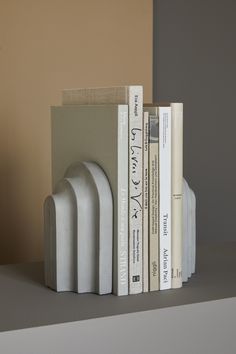 three books are stacked on top of each other in front of a beige wall and two white bookends