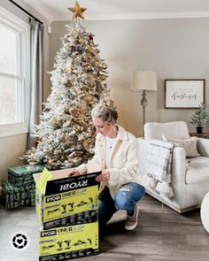 a woman sitting on the floor next to a christmas tree holding a box with instructions