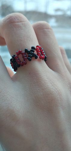 a woman's hand with a ring made out of black, red and white beads