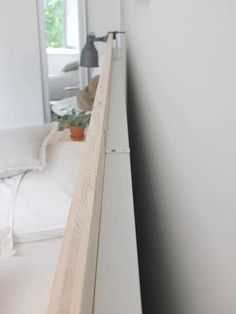 a white bed sitting under a window next to a wall mounted light on top of a wooden headboard