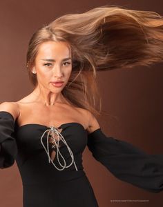 a woman in a black dress is holding her hair up and looking at the camera