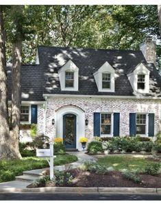 a brick house with blue shutters and trees in the front yard, surrounded by landscaping