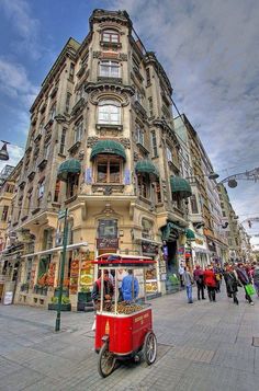 a red cart is parked in front of a tall building on a street with people walking by