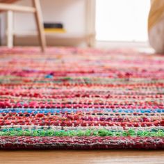 a multicolored rug on the floor with a chair and table in the background