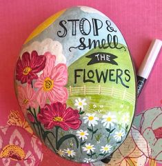 a rock with flowers painted on it and a marker next to it that says stop & smell the flowers