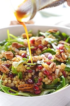 someone pouring dressing onto a salad in a white bowl