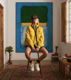 a woman is sitting on a chair in front of a painting and wearing white tennis shoes