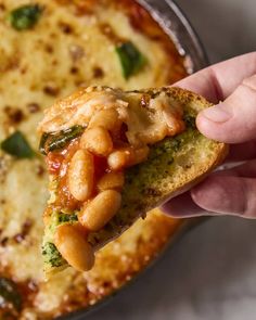 a hand holding up a piece of bread with beans and broccoli on it