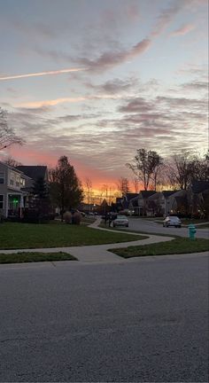 the sun is setting over some houses and cars on the street in front of them