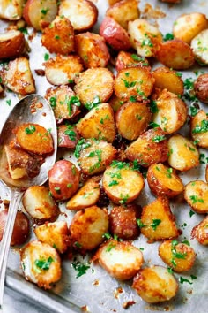 a pan filled with cooked potatoes and parsley next to a spoon on a table