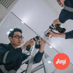 two men are working on a glass wall with an angle grinder and power drill