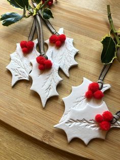 two christmas decorations are sitting on a cutting board with holly leaves and pom - poms