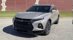 a silver chevrolet suv parked in front of a brick building with grass and bushes behind it