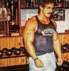 a man standing in front of a gym machine with his hands on the dumbs