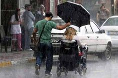 a man pushing a woman in a stroller with an umbrella on a city street