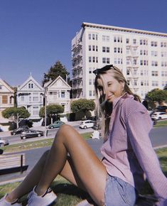 a beautiful young woman sitting on top of a grass covered field next to a park