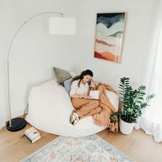 a woman is sitting on a bean bag chair in her living room reading a book