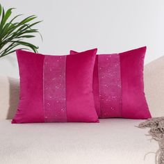 two pink pillows sitting on top of a white couch next to a potted plant