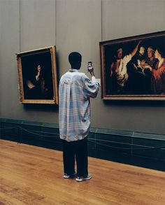 a man taking a photo of some paintings on the wall with his cell phone in front of him