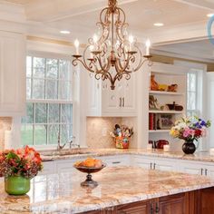 a chandelier hanging from the ceiling in a kitchen with marble counter tops and white cabinets