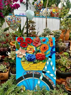 an art piece is sitting in the middle of many potted plants with flowers on them