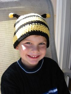 a young boy sitting in a chair wearing a knitted hat and smiling at the camera