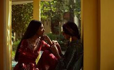 two women sitting next to each other in front of a window looking at each other