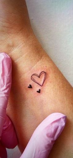 a small heart tattoo on the back of a woman's left arm, with hearts drawn