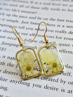 a pair of earrings with yellow flowers on them sitting on top of an open book