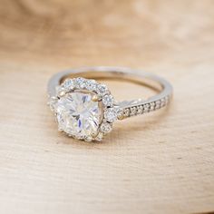 a white diamond ring on top of a wooden table with diamonds around the band and center stone