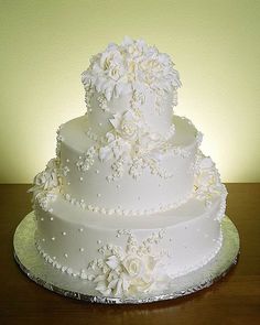 a three tiered white wedding cake with flowers on it's side, sitting on a wooden table