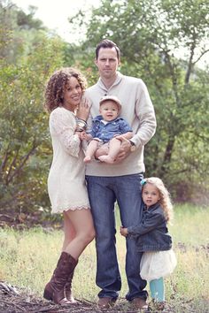 a man, woman and two children posing for a photo in a field with trees