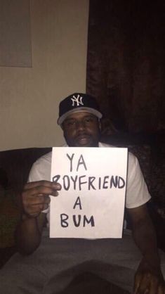 a man sitting on top of a couch holding a sign that says ya boyfriend a bum