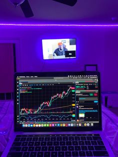 a laptop computer sitting on top of a table in front of a tv screen and purple lighting