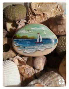 a rock with a sailboat painted on it surrounded by seashells and shells