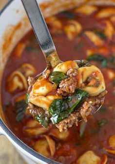 a ladle full of pasta and spinach soup being held up by a spoon