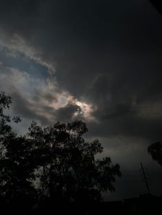 the sun is shining through dark clouds over trees