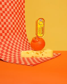 an orange sitting on top of a piece of cheese next to a can of cheddar