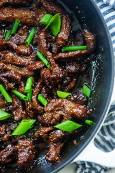 meat with green onions in a skillet on top of a white and blue towel