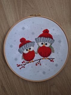 two red birds wearing knitted hats are sitting on a branch with snowflakes