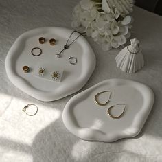 two white trays with rings and other jewelry on them next to a flower vase