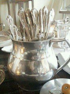 a silver pitcher filled with spoons on top of a table next to plates and utensils