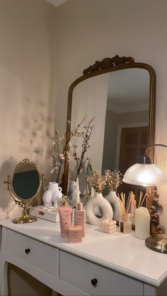 a white dresser topped with lots of different types of cosmetics and candles next to a mirror