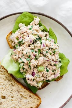 a white plate topped with a salad next to a slice of bread