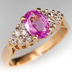 This sweet ring is centered with an oval cut pink sapphire, weighing 1.00 carat, in a four-prong setting. The shoulders are each bead set with six (6) round brilliant cut diamonds. The ring measures 6.9mm at the top, rises 6.3mm above the finger, tapering to 2.0mm wide and 0.7mm thick at the base of the shank. The ring currently fits a size 4.75. Luxury Pink Gold Sapphire Ring As Gift, Classic Pink Diamond Ring With Round Cut, Classic Pink Sapphire Ring For Anniversary, Classic Pink Round Cut Diamond Ring, Classic Pink Diamond Ring With Accents, Classic Pink Sapphire Ring For Wedding, Classic Pink Diamond Ring With Center Stone, Pink Oval Diamond Ring With Center Stone, Pink Sapphire Ring With Diamond Accents Round Cut