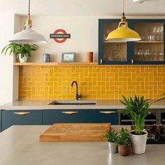 a kitchen with yellow and blue cabinets, potted plants on the counter top and hanging lights over the sink